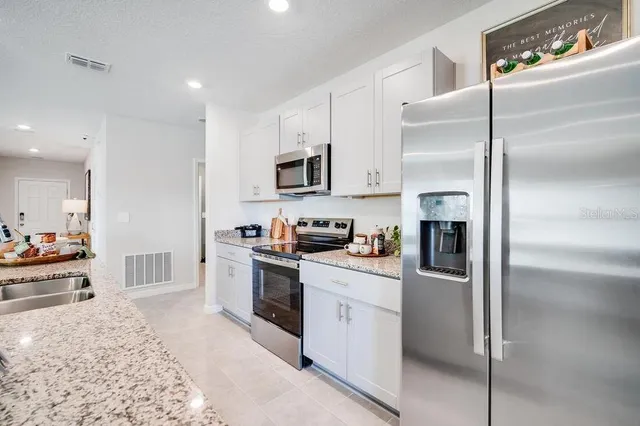 a kitchen with stainless steel appliances kitchen island granite countertop a dining table chairs stove refrigerator and cabinets