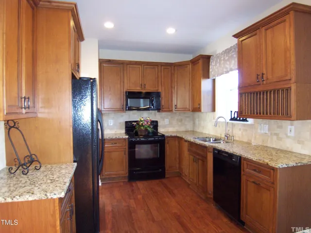 a kitchen with stainless steel appliances granite countertop a refrigerator a sink dishwasher a stove and a oven with wooden floor