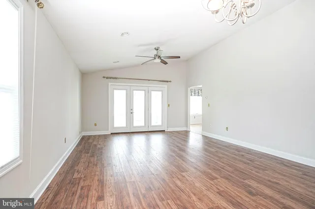 an empty room with wooden floor ceiling fan and windows