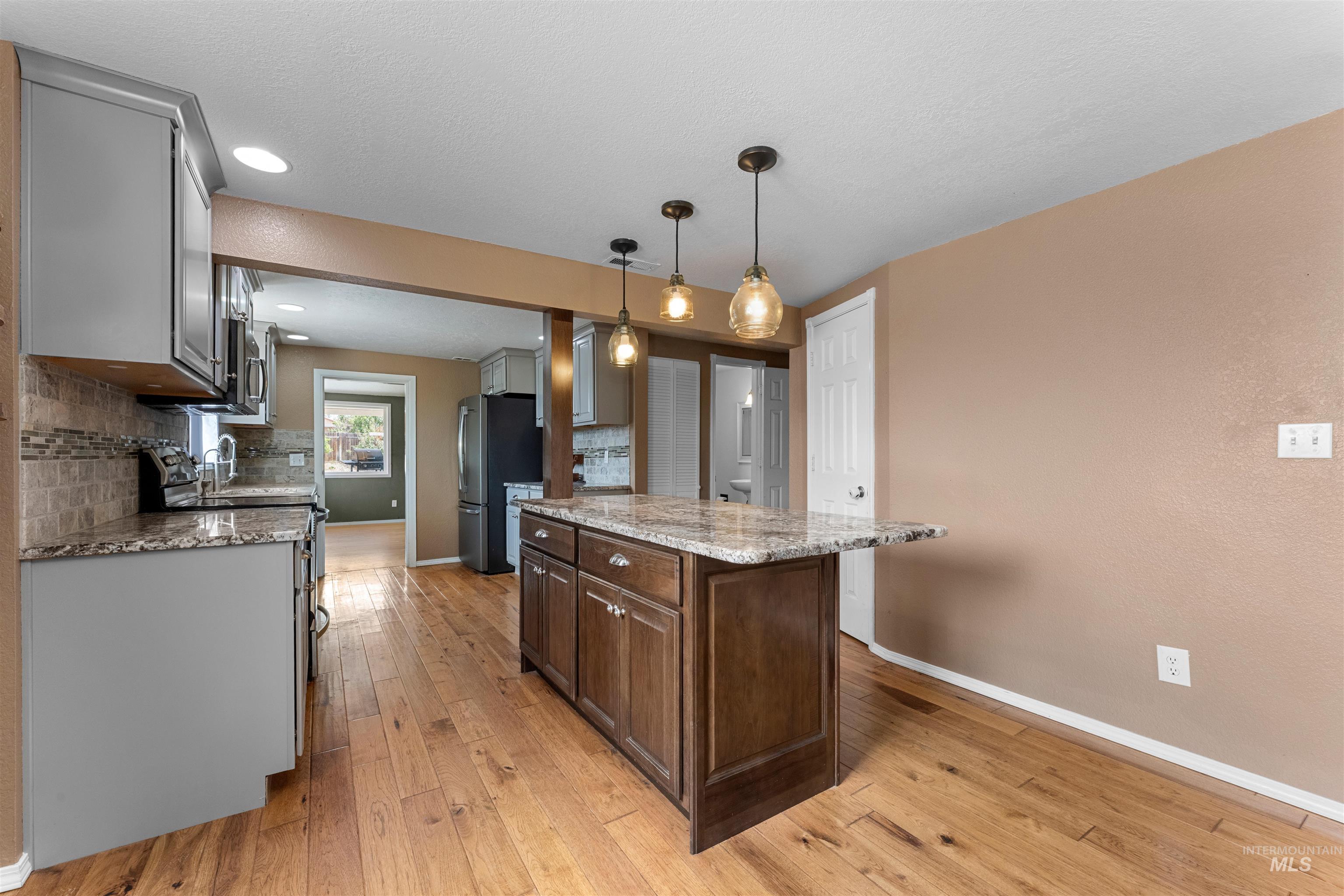 17441 Upper Pleasant Ridge Road Caldwell, ID 83607 - Photo 10 of 40 Open-concept kitchen featuring an island with pendant lighting, wood-finish flooring, granite countertops, and tile backsplash