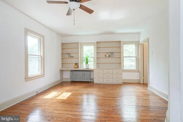 a view of empty room with wooden floor and fan