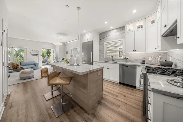 a kitchen with stainless steel appliances granite countertop a stove top oven a sink dishwasher and white cabinets with wooden floor