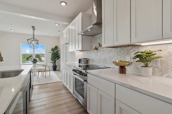 a kitchen with stainless steel appliances granite countertop a stove a sink a refrigerator and white cabinets with wooden floor