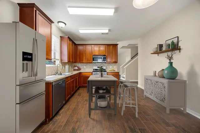 a kitchen with stainless steel appliances granite countertop a refrigerator a sink dishwasher a stove and white countertops with wooden floor
