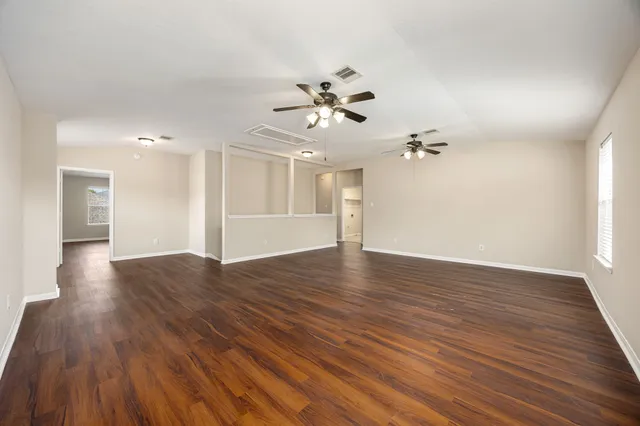 a view of an empty room with wooden floor and a ceiling fan