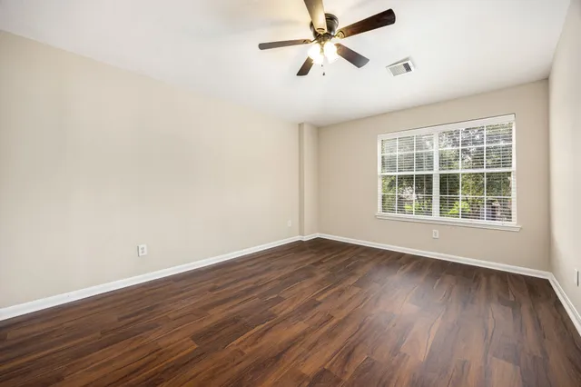 an empty room with wooden floor fan and windows