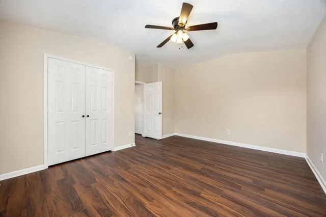 an empty room with wooden floor chandelier fan and windows