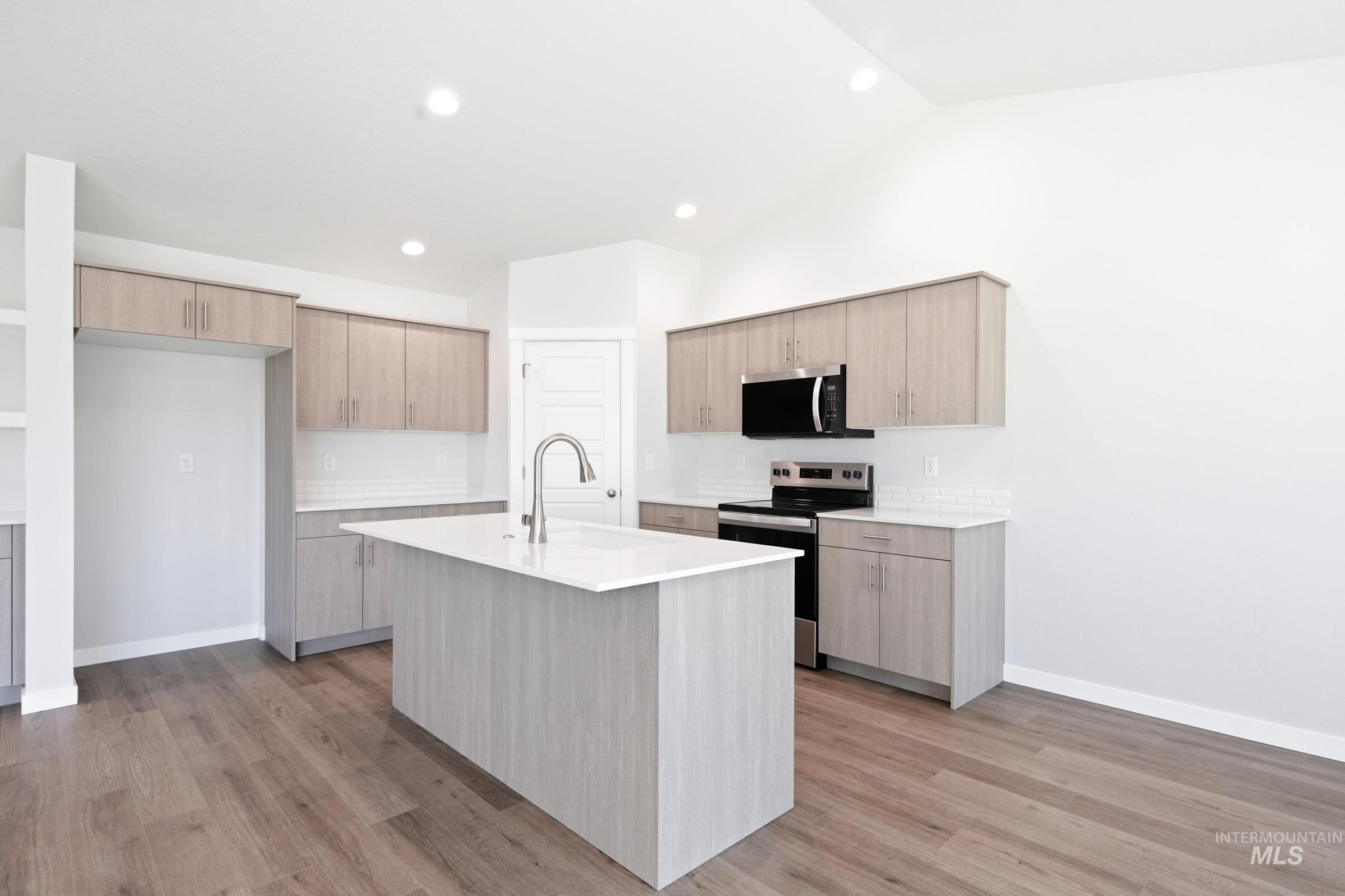 12877 Decatur Street Nampa, ID 83651 - Photo 7 of 22 Open-concept kitchen featuring an expansive island with an undermount sink and gooseneck faucet, light wood-finish cabinetry, white countertops, and wood-finish flooring