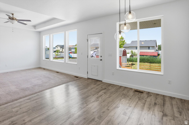 3636 West 910 South Syracuse, UT 84075 - Photo 40 of 70 Spacious open-concept room featuring light wood-finish flooring, a tray ceiling with a ceiling fan, and large windows