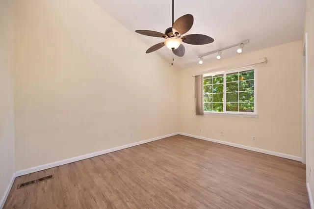 an empty room with wooden floor chandelier fan and windows
