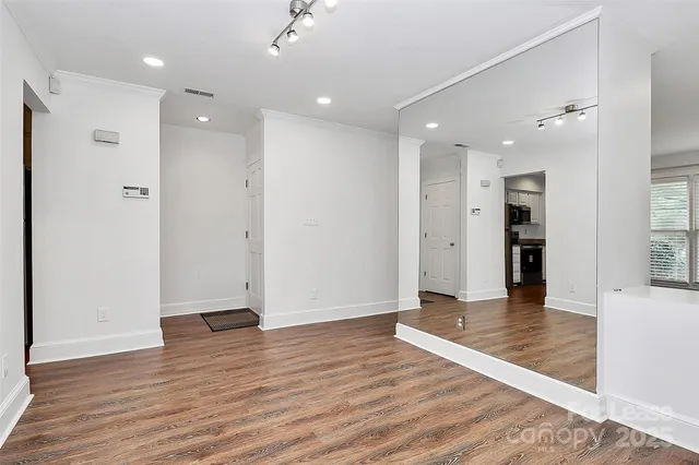 a view of an empty room with wooden floor and a kitchen
