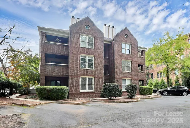 a view of a brick house with a yard plants and large tree