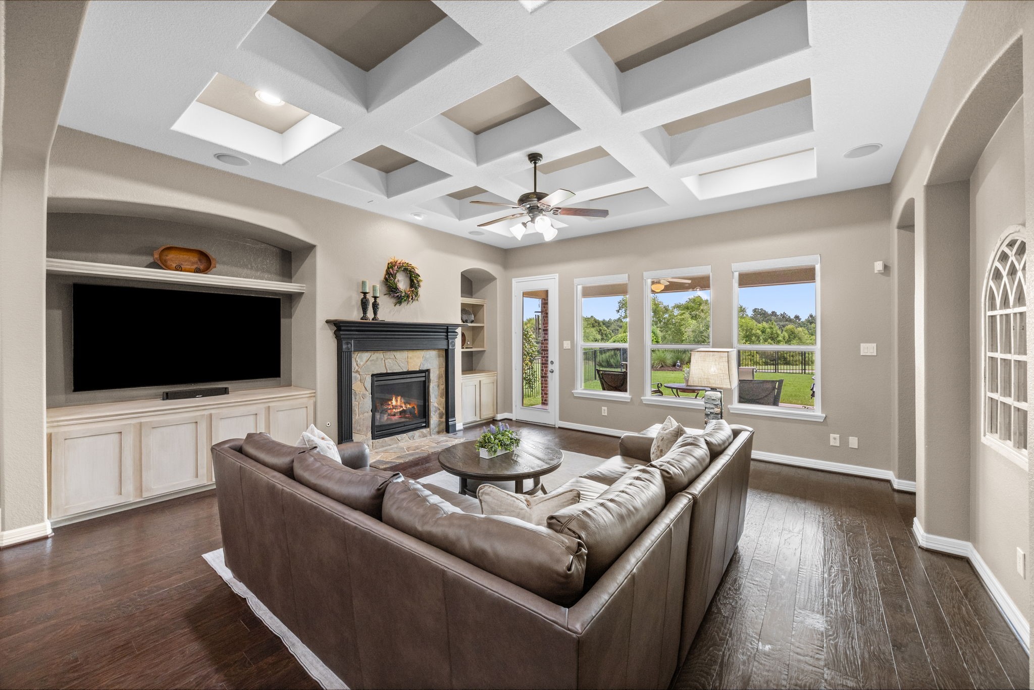 27642 Linden Ridge Lane Fulshear, TX 77441 - Photo 14 of 42 The Family Room is absolutely gorgeous, featuring a coffered ceiling, rich wood flooring, and a cozy gas-log Fireplace with a custom mantel and stone surround. Built-in shelving on both sides includes one larger niche designed to accommodate your TV, offering both style and functionality. A wall of windows fills the space with natural light while showcasing stunning views of the peaceful nature reserve, creating a warm and inviting setting for everyday living and entertaining.