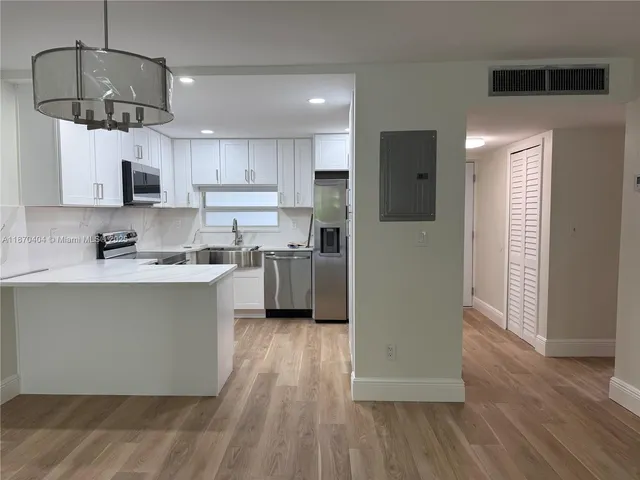 a kitchen with stainless steel appliances a refrigerator a sink dishwasher a stove and white cabinets with wooden floor