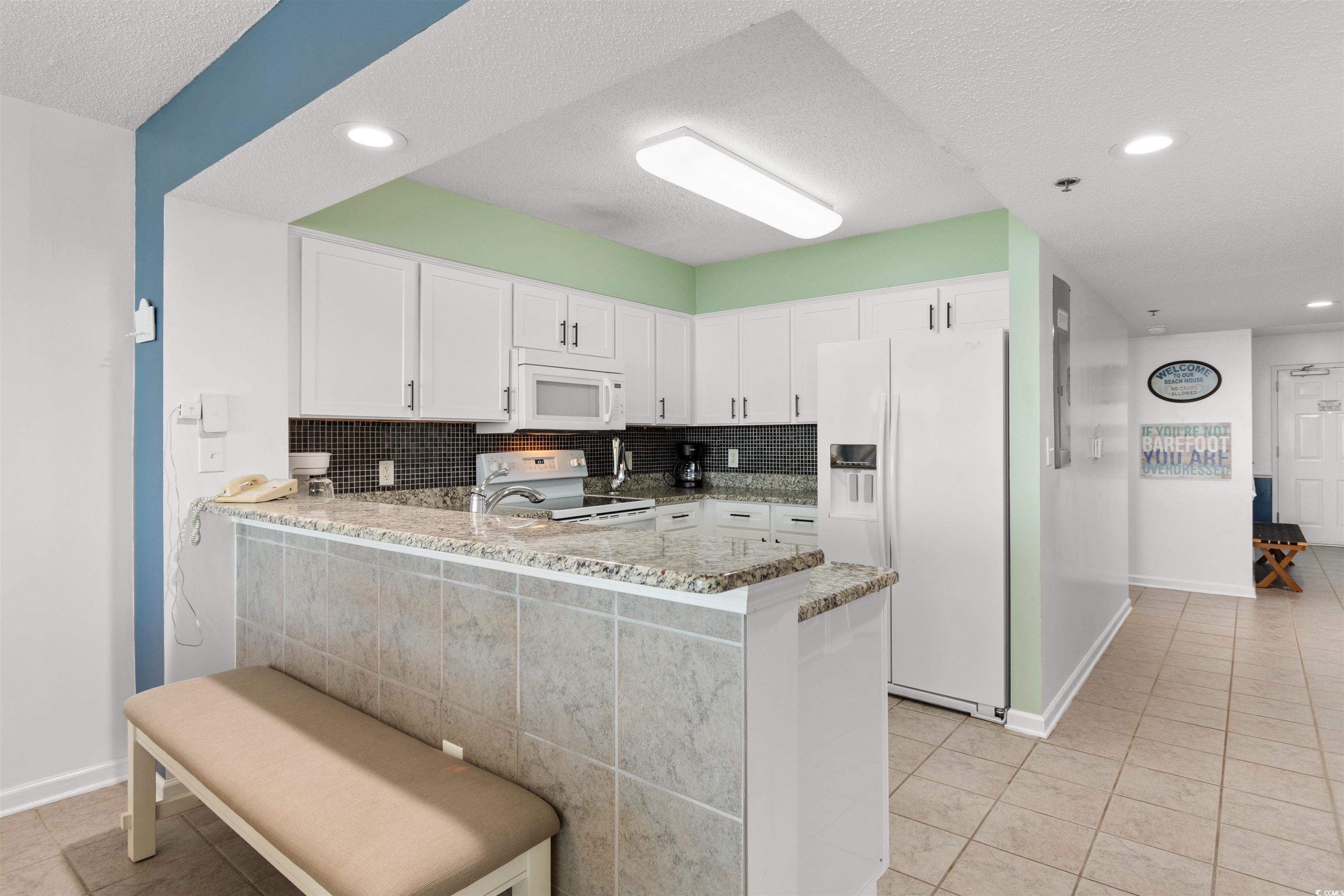 1625 South Ocean Boulevard, Unit 1603 North Myrtle Beach, SC 29582 - Photo 9 of 39 Kitchen featuring tasteful backsplash, a textured ceiling, a peninsula, light stone counters, and white appliances