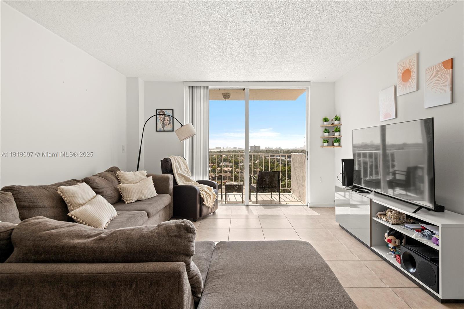2350 Northeast 135th Street, Unit 1006 North Miami, FL 33181 - Photo 4 of 29 a living room with furniture a flat screen tv and a floor to ceiling window