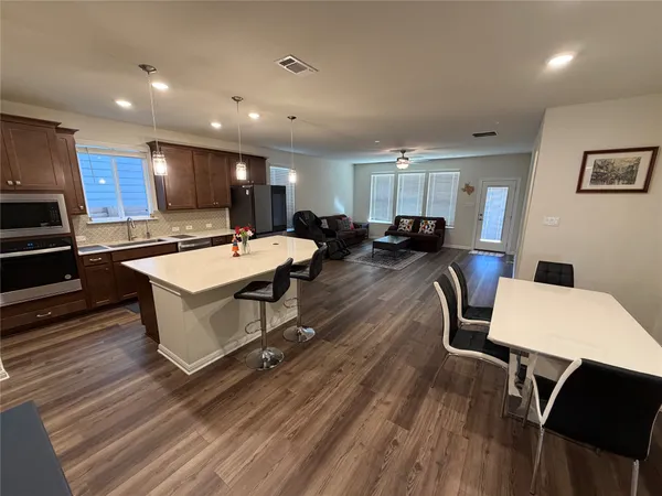a living room with stainless steel appliances furniture a table and a kitchen view