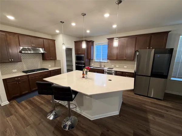 a large kitchen with stainless steel appliances a large counter top and wooden floors