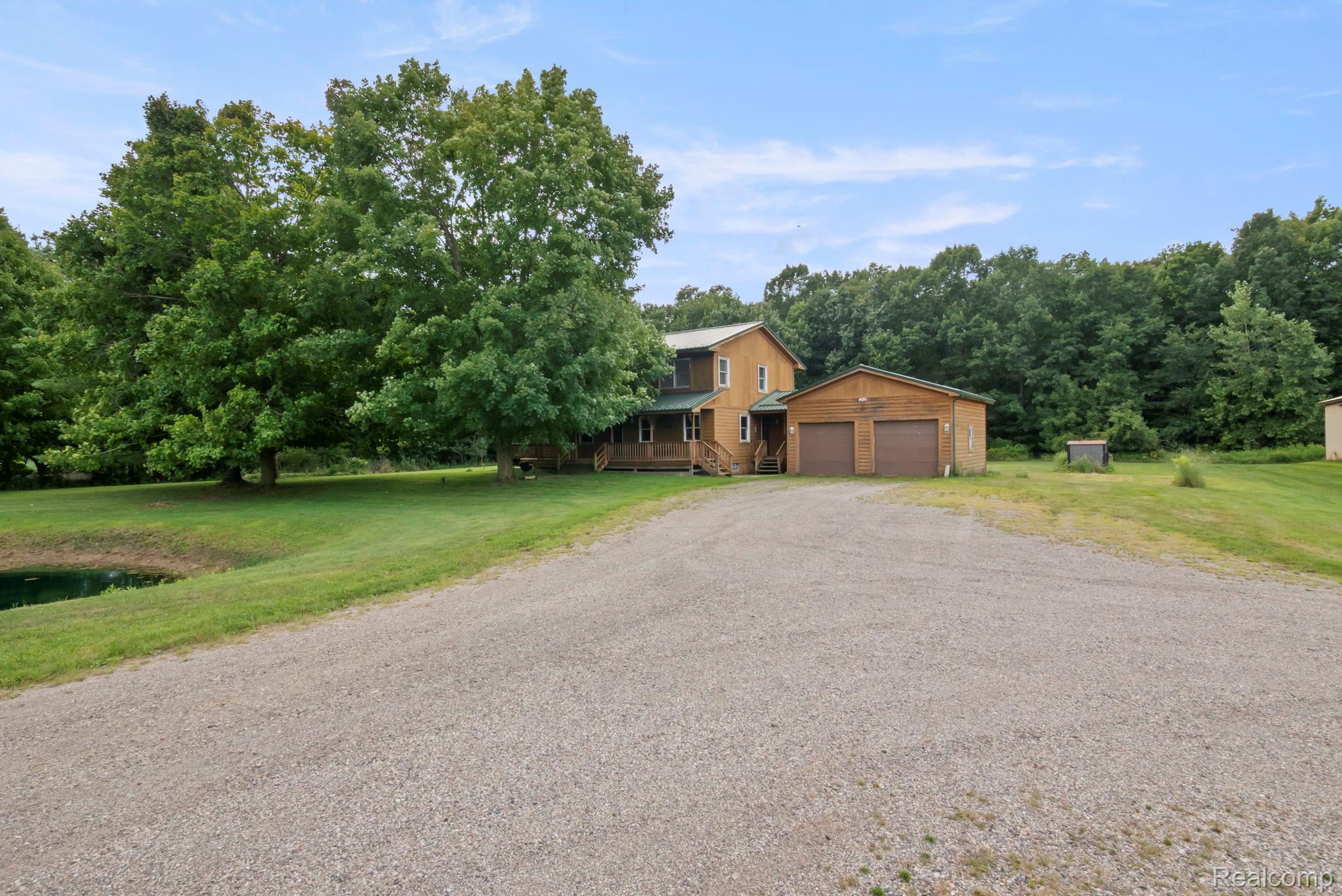 76565 McFadden Road Armada, MI 48005 - Photo 82 of 95 Two-story siding residence with an attached two-car garage, gravel driveway, and a pond feature