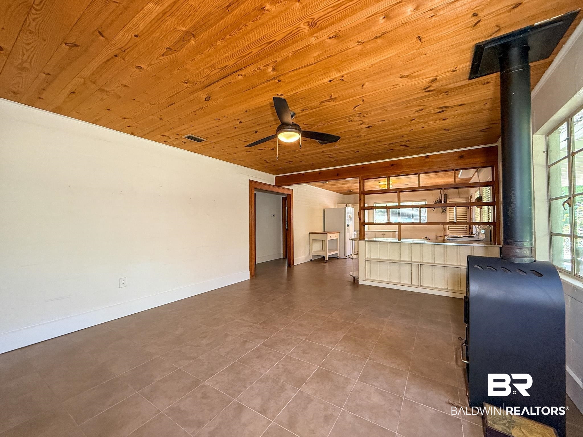 18711 Keller Road Foley, AL 36535 - Photo 6 of 38 Room featuring a wood-panel ceiling, dark tile flooring, and a freestanding stove with a black stovepipe