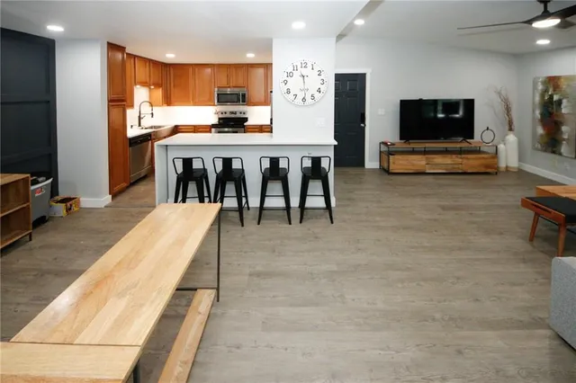 a living room with stainless steel appliances furniture a flat screen tv and a kitchen view