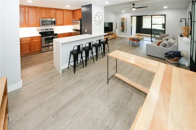 a living room with stainless steel appliances kitchen island granite countertop a refrigerator a stove a sink a dining table and chairs with wooden floor