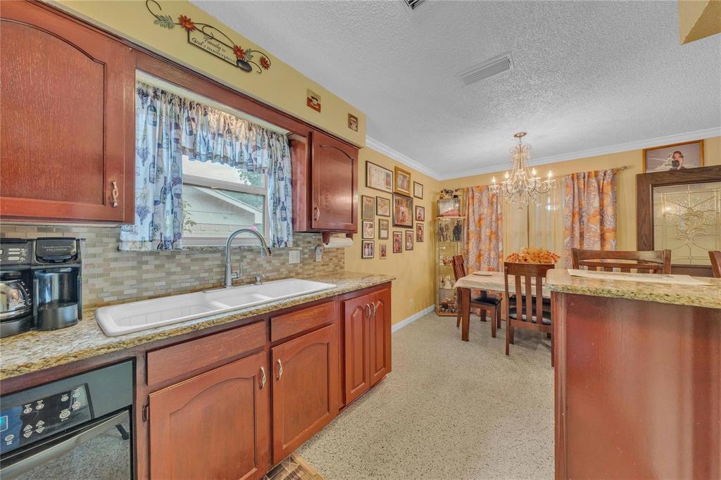 7613 Clover Lane Watauga, TX 76148 - Photo 13 of 36 Kitchen with light stone countertops, suspended lighting, crown molding, tasteful backsplash, and a textured ceiling