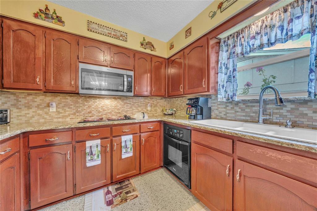 7613 Clover Lane Watauga, TX 76148 - Photo 14 of 36 Kitchen featuring wood finish cabinets, stainless steel microwave, black oven, light stone counters, and a textured ceiling