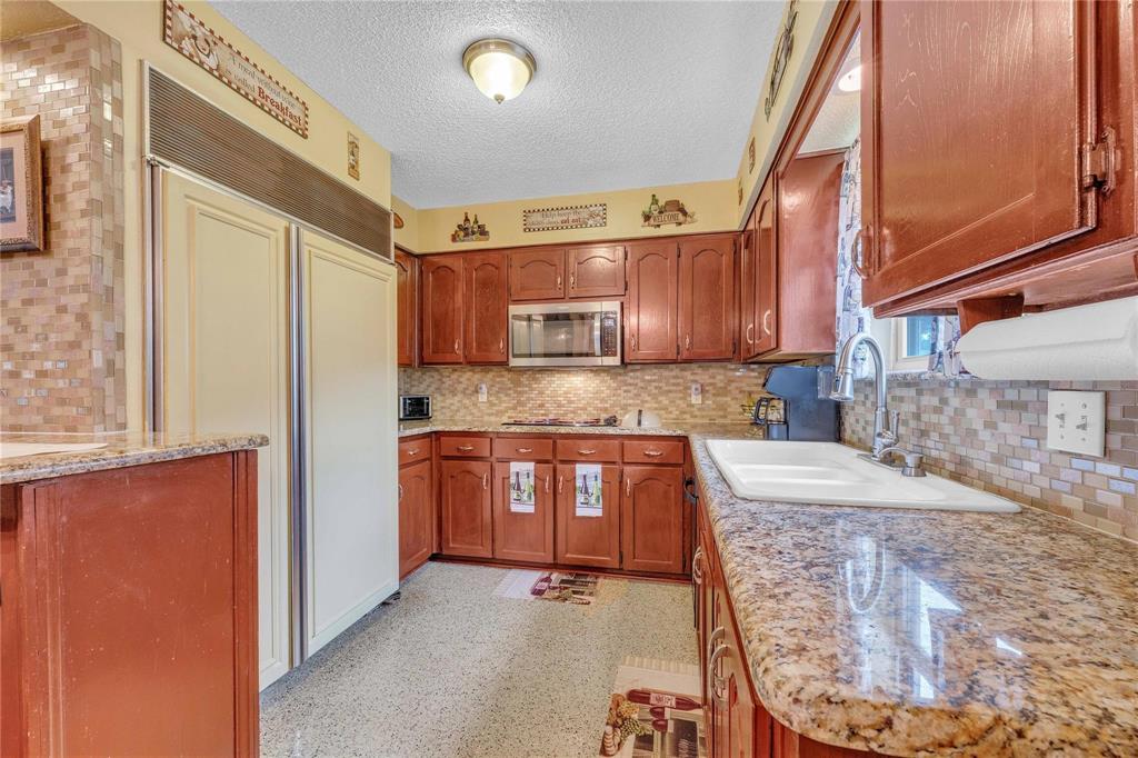 7613 Clover Lane Watauga, TX 76148 - Photo 15 of 36 Kitchen featuring stainless steel appliances, wood finish cabinetry, light stone counters, a textured ceiling, and tasteful backsplash