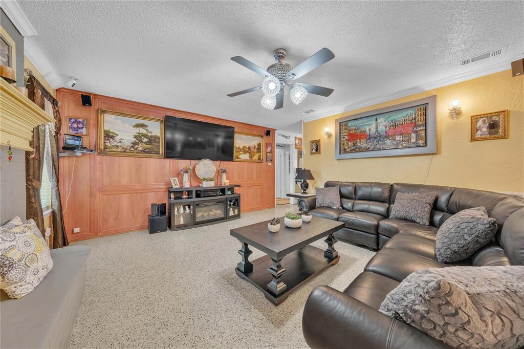 7613 Clover Lane Watauga, TX 76148 - Photo 8 of 36 Living room featuring a fireplace, speckle patterned floor, ornamental molding, a ceiling fan, and a textured ceiling