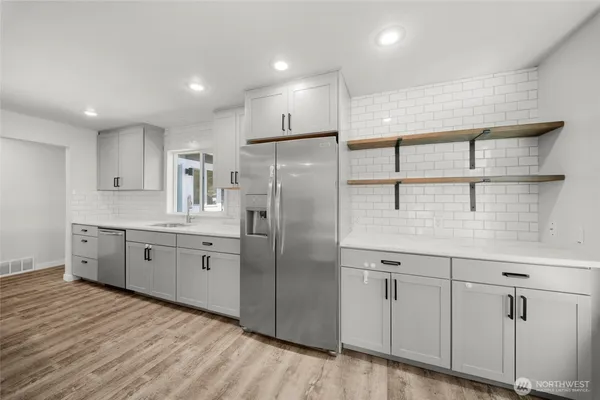 a large kitchen with stainless steel appliances granite countertop a refrigerator a sink dishwasher and white cabinets with wooden floor