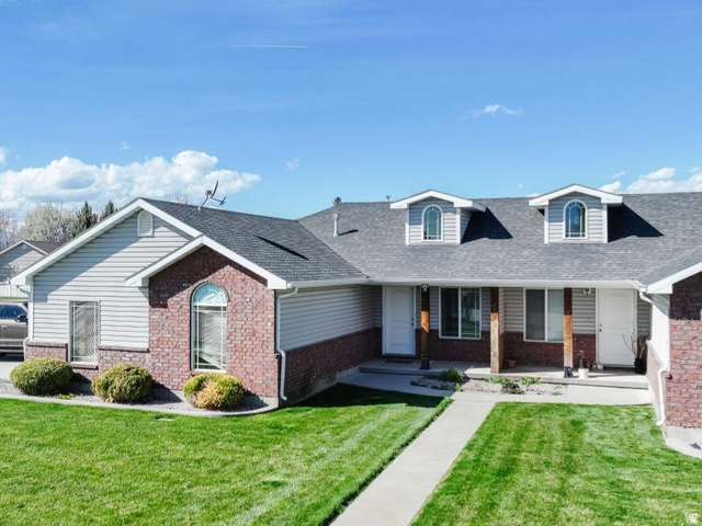 619 East 1st S Street, Unit S Preston, ID 83263 - Photo 12 of 16 Front exterior featuring gray siding, red brick accents, two dormer windows with arched tops, a covered porch entry with wood-wrapped columns, and a concrete walkway