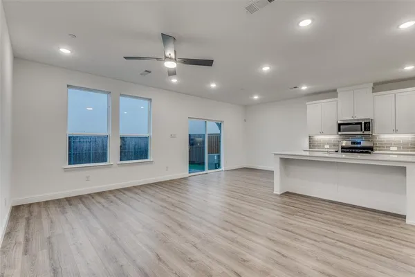 a view of an empty room with wooden floor and a kitchen