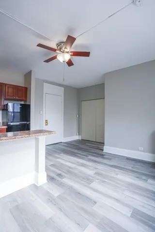 a view of kitchen and empty room with wooden floor and fan