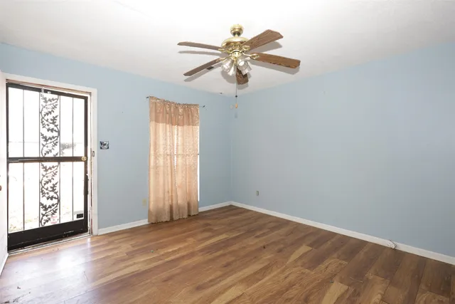 an empty room with wooden floor fan and windows