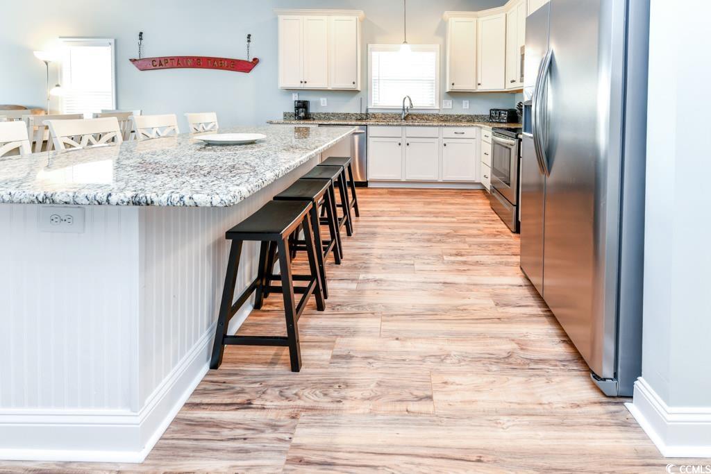 1614 North Ocean Boulevard Surfside Beach, SC 29575 - Photo 3 of 38 Kitchen with a sink, light wood-style floors, appliances with stainless steel finishes, white cabinetry, and a kitchen breakfast bar