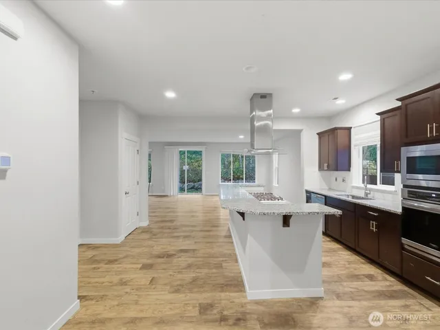 a large white kitchen with kitchen island a sink wooden floor and stainless steel appliances