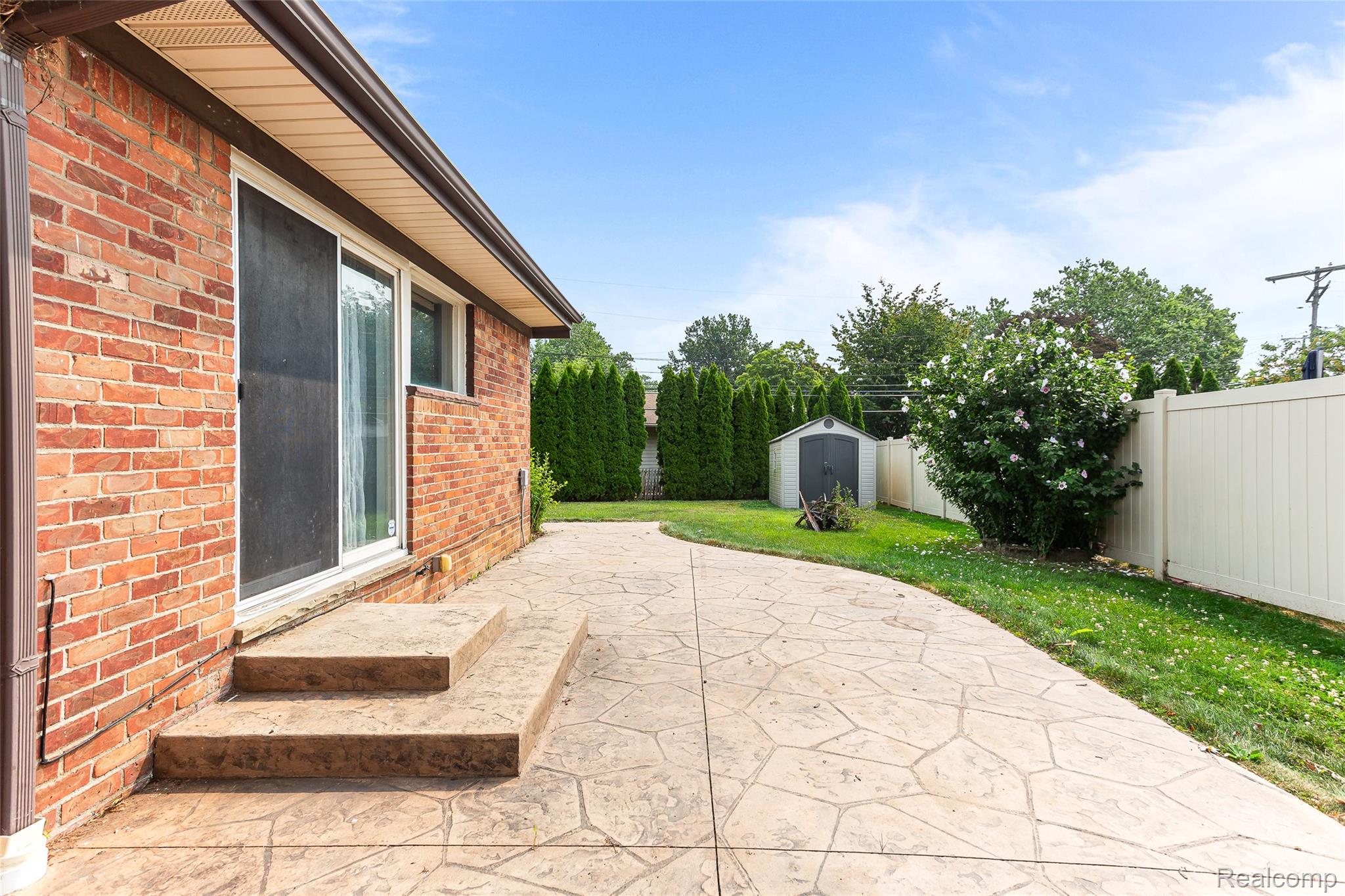 2345 Middlefield Road Trenton, MI 48183 - Photo 34 of 42 Expansive backyard featuring a stamped concrete patio, brick exterior, sliding glass door, mature landscaping, and a storage shed