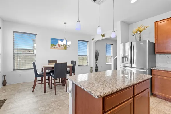 a kitchen with granite countertop kitchen island stainless steel appliances a table chairs sink and refrigerator