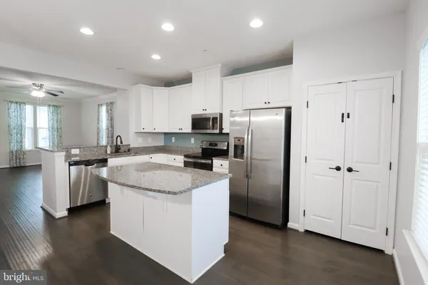 a kitchen with stainless steel appliances granite countertop a refrigerator a stove a sink and white cabinets with wooden floor