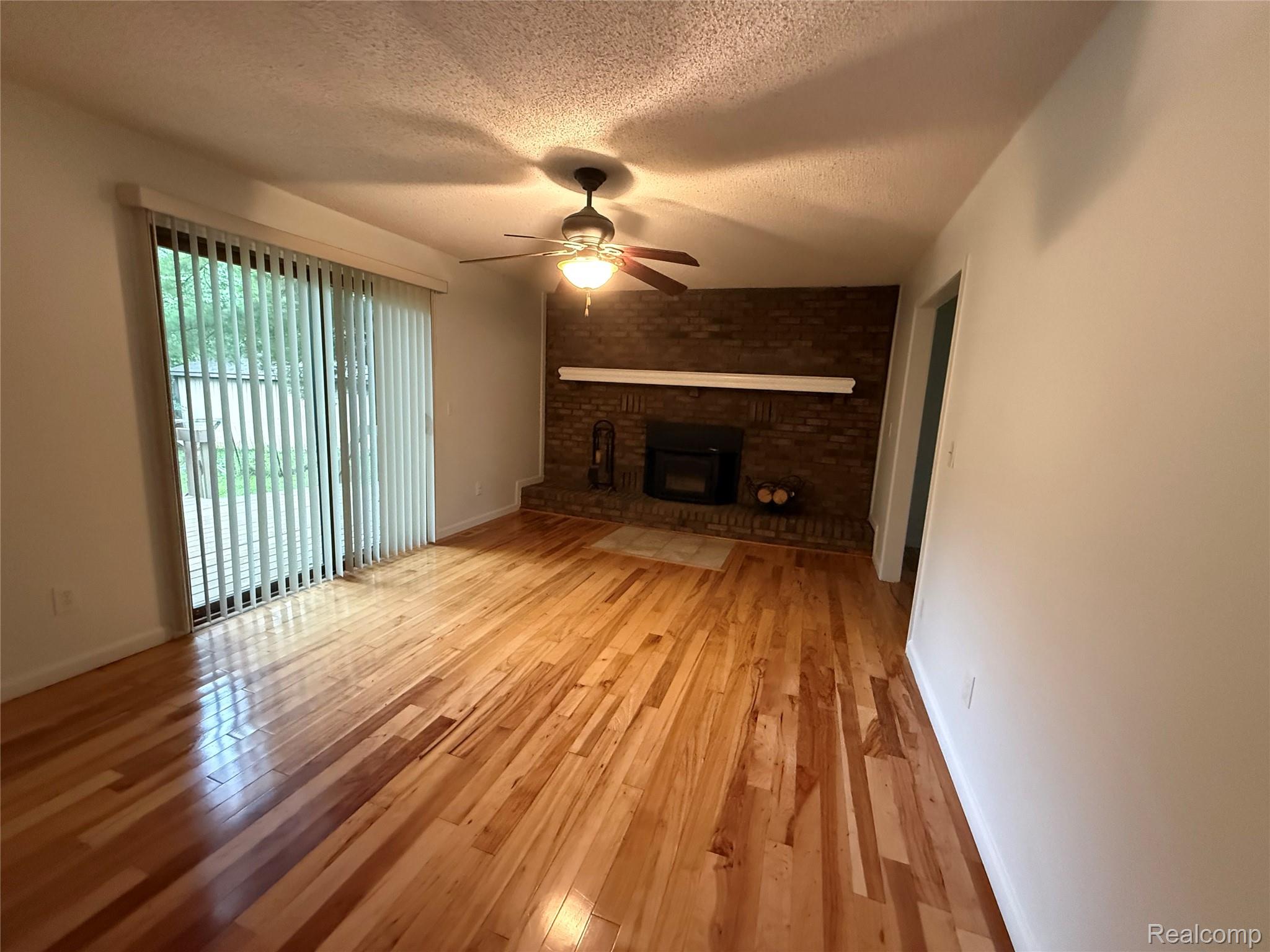 10280 Nimphie Road Fenton, MI 48430 - Photo 6 of 30 Wood-finish flooring with a brick-faced fireplace, white mantel, and ceiling fan with integrated lighting