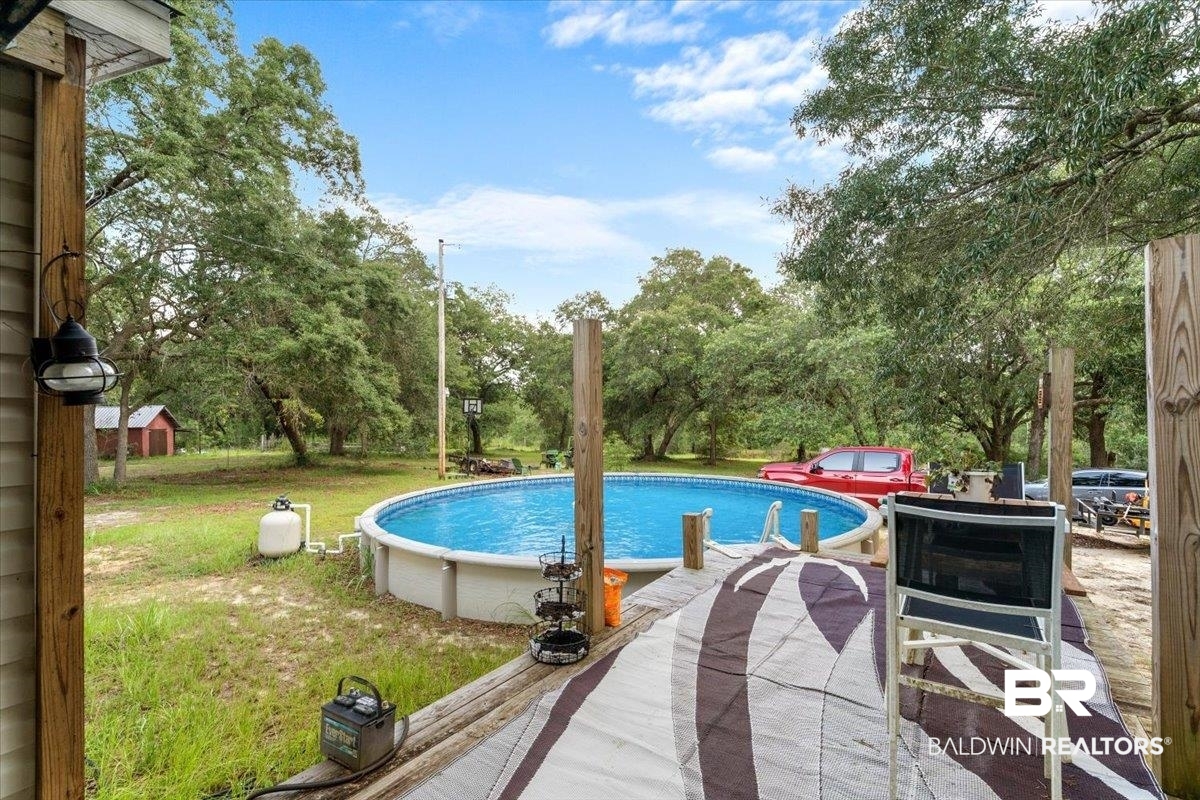 21011 River Road Robertsdale, AL 36567 - Photo 20 of 29 Expansive outdoor space featuring a large above-ground pool with surrounding decking, mature trees, and a distant red shed