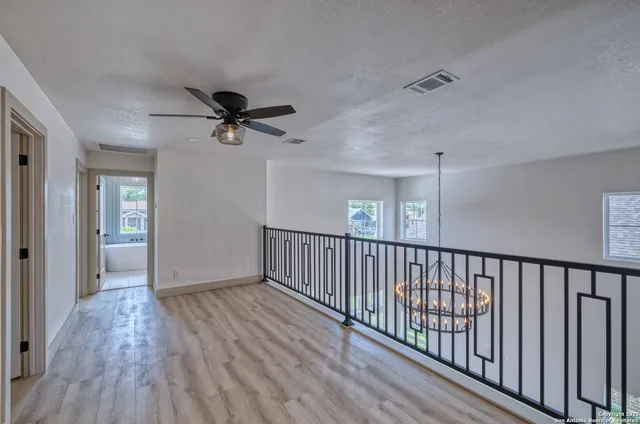 a view of an empty room with wooden floor and a ceiling fan