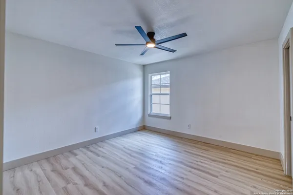 an empty room with wooden floor ceiling fan and windows
