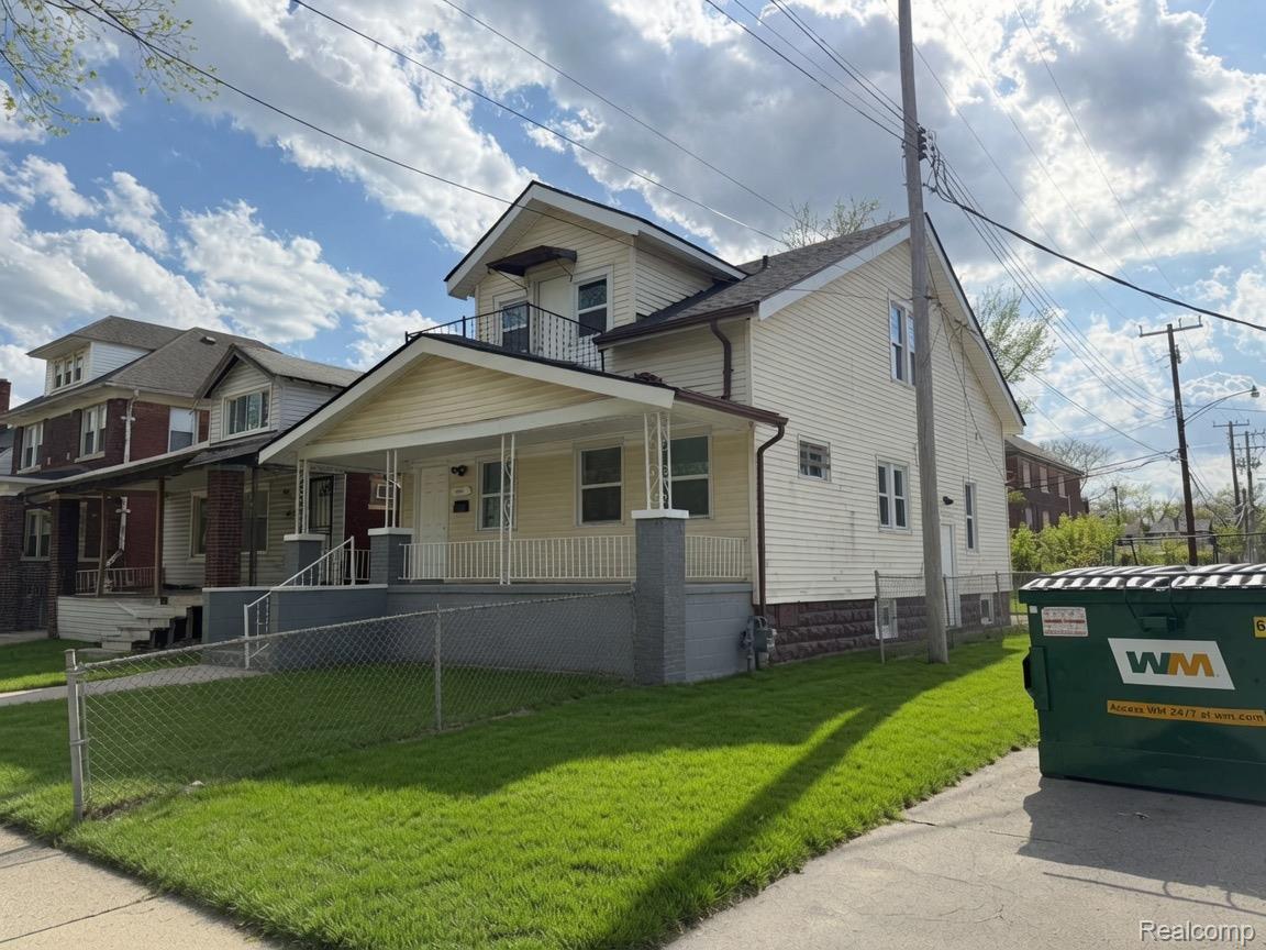 15935 Normandy Street Detroit, MI 48238 - Photo 1 of 28 Two-story residential property featuring a covered front porch with white railings and columns, a second-story balcony with dark railings, a white siding exterior, and a chain-link fence enclosing the front yard