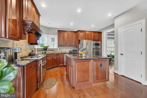 a kitchen with stainless steel appliances granite countertop a stove a sink dishwasher and a refrigerator with wooden floor