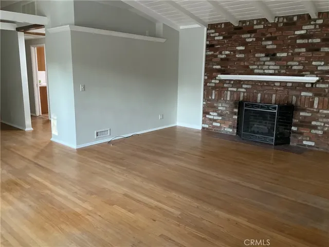 a view of an empty room with wooden floor and a fireplace