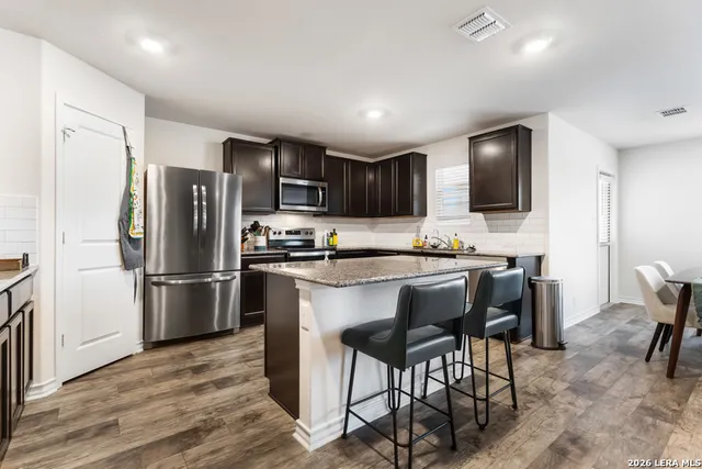 a kitchen with stainless steel appliances granite countertop a refrigerator a stove a sink a dining table and chairs