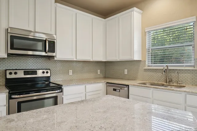 a kitchen with granite countertop a sink a stove a refrigerator and cabinets