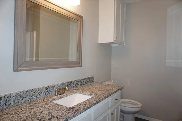 a bathroom with a granite countertop sink a toilet and a mirror